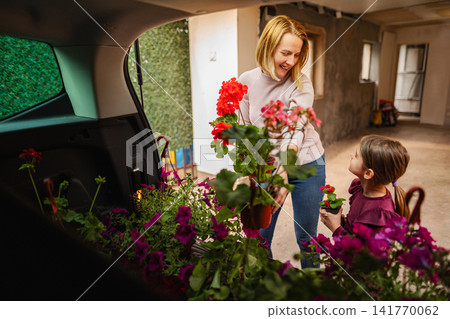 Mother and daughter unloading blooming flowers from car trunk Mother and daughter unloading blooming flowers from car trunk 141770062
