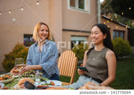 Multi ethnic women friends enjoying outdoor backyard dinner party Multi ethnic women friends enjoying outdoor backyard dinner party 141770084