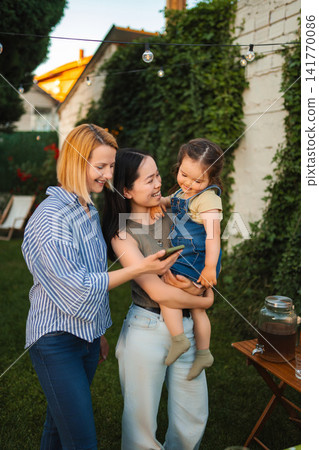 Two mothers and child watching phone together in backyard Two mothers and child watching phone together in backyard 141770086
