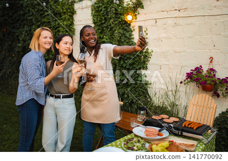Diverse women friends enjoying backyard barbecue party taking selfie Diverse women friends enjoying backyard barbecue party taking selfie 141770092