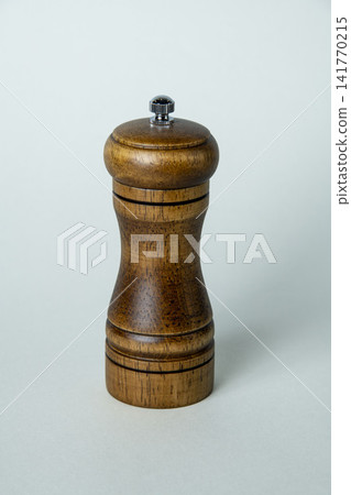 A studio shoot with a white background, showing someone grinding spices with a wooden pepper mill. A studio shoot with a white background, showing someone grinding spices with a wooden pepper mill. 141770215
