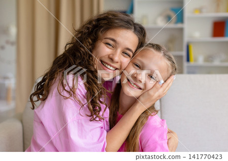 Smiling mother embracing her little daughter and smiling at camera together Smiling mother embracing her little daughter and smiling at camera together 141770423