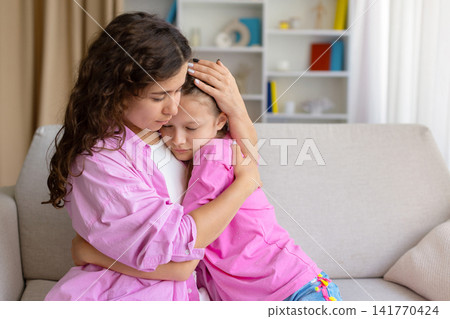 Caring mother holding and comforting her sad daughter on the sofa Caring mother holding and comforting her sad daughter on the sofa 141770424