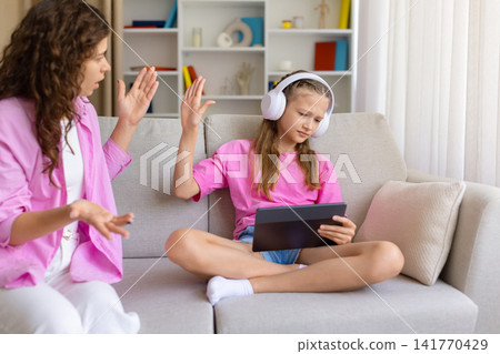 Annoyed mother arguing with her daughter wearing headphones and ignoring her Annoyed mother arguing with her daughter wearing headphones and ignoring her 141770429