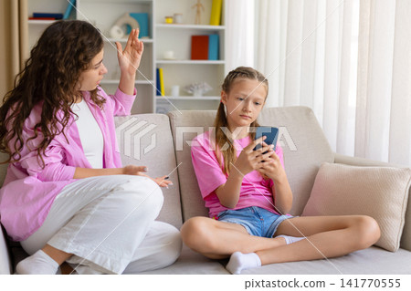 Frustrated mother scolding daughter, who ignores her and stays focused on smartphone Frustrated mother scolding daughter, who ignores her and stays focused on smartphone 141770555