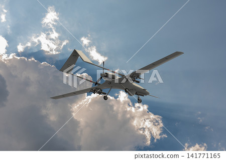 Armed unmanned aerial vehicle flying beneath a bright blue sky with large clouds and sunlight. Armed unmanned aerial vehicle flying beneath a bright blue sky with large clouds and sunlight. 141771165