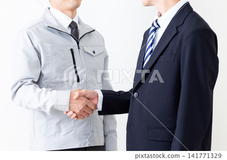 A young man in a business suit and a middle-aged man in work clothes shake hands. A young man in a business suit and a middle-aged man in work clothes shake hands. 141771329