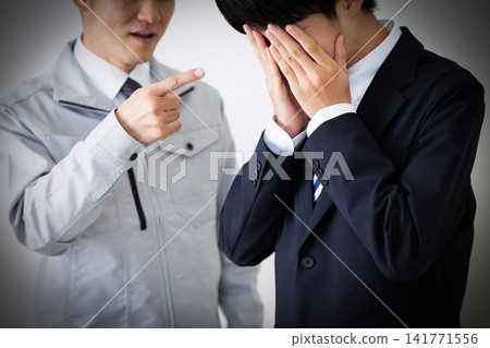 A young man in a business suit and a middle-aged man in work clothes, both looking dejected after being scolded. A young man in a business suit and a middle-aged man in work clothes, both looking dejected after being scolded. 141771556