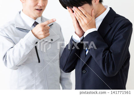 一位身穿西裝的年輕男子和一位身穿工作服的中年男子,兩人都被訓斥後都顯得垂頭喪氣。 一位身穿西裝的年輕男子和一位身穿工作服的中年男子,兩人都被訓斥後都顯得垂頭喪氣。 141771561