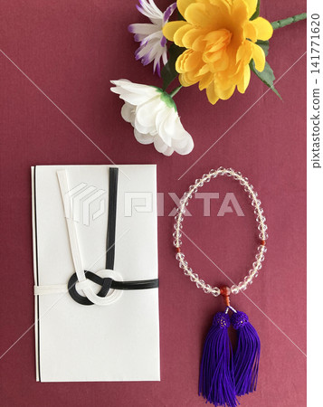 A condolence envelope, prayer beads, and floral tribute are placed against a maroon background. A condolence envelope, prayer beads, and floral tribute are placed against a maroon background. 141771620