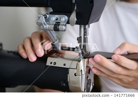 A Japanese man in his 30s sewing leather with an industrial sewing machine. A Japanese man in his 30s sewing leather with an industrial sewing machine. 141771666