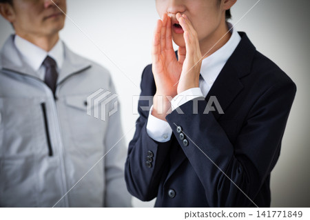 一個穿著西裝的年輕男子和一個穿著工作服的中年男子正在背後說出老闆的壞話。 一個穿著西裝的年輕男子和一個穿著工作服的中年男子正在背後說出老闆的壞話。 141771849