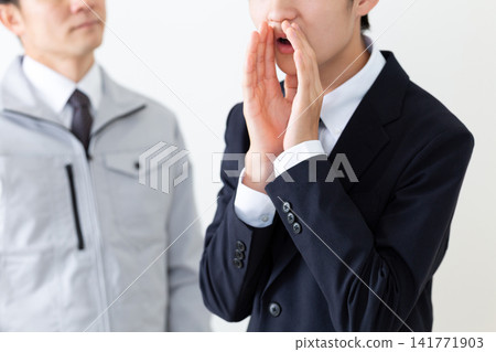 一個穿著西裝的年輕男子和一個穿著工作服的中年男子正在背後說出老闆的壞話。 一個穿著西裝的年輕男子和一個穿著工作服的中年男子正在背後說出老闆的壞話。 141771903