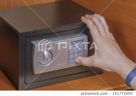Man hand enters combination PIN code on electronic safe box digital keypad panel inside wooden cabinet shelf for secure personal item access management system Man hand enters combination PIN code on electronic safe box digital keypad panel inside wooden cabinet shelf for secure personal item access management system 141772005