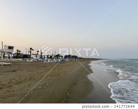 Tourist recreation area, beach umbrellas, beach loungers. Picturesque beach, waves crashing on the sandy shore. Cyprus Island, Mediterranean Sea. Tourist recreation area, beach umbrellas, beach loungers. Picturesque beach, waves crashing on the sandy shore. Cyprus Island, Mediterranean Sea. 141772644