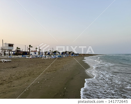 Tourist recreation area, beach umbrellas, beach loungers. Picturesque beach, waves crashing on the sandy shore. Cyprus Island, Mediterranean Sea. Tourist recreation area, beach umbrellas, beach loungers. Picturesque beach, waves crashing on the sandy shore. Cyprus Island, Mediterranean Sea. 141772645