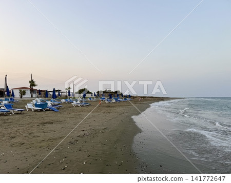 Tourist recreation area, beach umbrellas, beach loungers. Picturesque beach, waves crashing on the sandy shore. Cyprus Island, Mediterranean Sea. Tourist recreation area, beach umbrellas, beach loungers. Picturesque beach, waves crashing on the sandy shore. Cyprus Island, Mediterranean Sea. 141772647