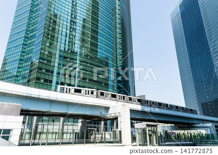 Low-angle view of a New Transit Yurikamome line train running on the elevated track with modern skyscrapers in Shiodome, Minato, Tokyo, Japan. It's an automated guideway transit service in Tokyo. Low-angle view of a New Transit Yurikamome line train running on the elevated track with modern skyscrapers in Shiodome, Minato, Tokyo, Japan. It's an automated guideway transit service in Tokyo. 141772875