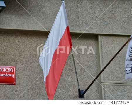 Krakow, Poland - August 6, 2023: Polish Flag and Podbrzezie Gallery Flag Near University Facade 141772979