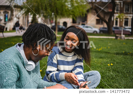 Happy young women bonding and laughing together in city park Happy young women bonding and laughing together in city park 141773472