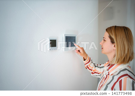 Woman adjusting smart home thermostat control panel Woman adjusting smart home thermostat control panel 141773498
