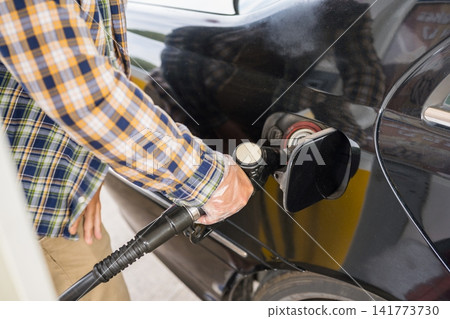 Man driver refueling black car at gas station Man driver refueling black car at gas station 141773730