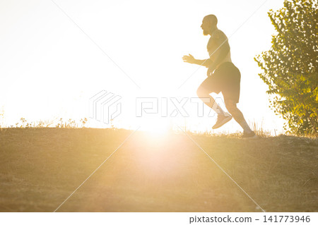 Man running up a hill during sunrise with bright light shining behind him Man running up a hill during sunrise with bright light shining behind him 141773946