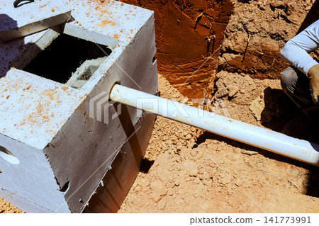 Workers dig hole for septic tank while preparing plumbing at construction site Workers dig hole for septic tank while preparing plumbing at construction site 141773991