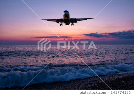 Passenger airliner landing over the ocean against the backdrop of scenic sunset sky Passenger airliner landing over the ocean against the backdrop of scenic sunset sky 141774135