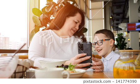 Mother Shares Smile. Shared Moment Over Breakfast. Mother And Son Enjoy Social Browsing Together. Mother And Her Son Happily Explore Social Media Amid Cozy Cafe Ambiance During Breakfast Mother Shares Smile. Shared Moment Over Breakfast. Mother And Son Enjoy Social Browsing Together. Mother And Her Son Happily Explore Social Media Amid Cozy Cafe Ambiance During Breakfast 141774390
