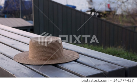 Quiet Summer Day With Hat. Relaxing Day With Straw Hat Outdoors. Peaceful Retreat In Backyard With Summer Accessories. Tranquil Summer Setting Featuring Straw Hat On Wooden Bench In Backyard Quiet Summer Day With Hat. Relaxing Day With Straw Hat Outdoors. Peaceful Retreat In Backyard With Summer Accessories. Tranquil Summer Setting Featuring Straw Hat On Wooden Bench In Backyard 141774437