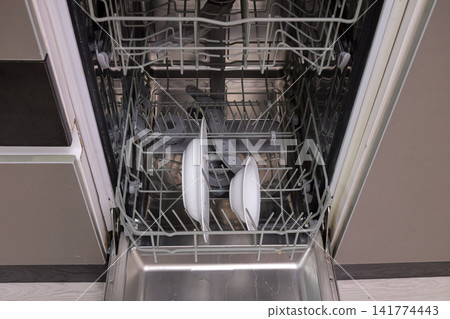 Stacked Plates In Dishwasher With Reflective Surfaces. Gray Kitchen With Dishes Drying In Tidy Setting. Interior Of Dishwasher With Porcelain Dishes And Soft Lighting After Meal Cleanup 141774443
