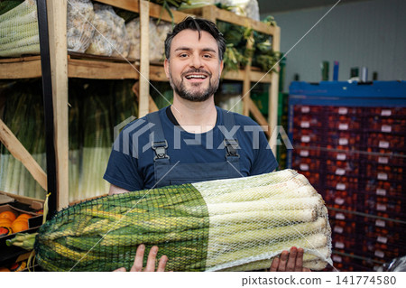 Smiling man handling fresh leeks in produce warehouse Smiling man handling fresh leeks in produce warehouse 141774580