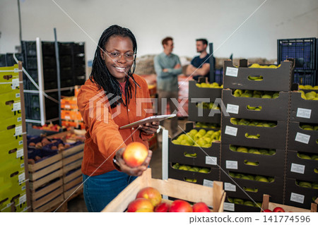 Woman inspecting apples in wholesale fruit distribution warehouse Woman inspecting apples in wholesale fruit distribution warehouse 141774596