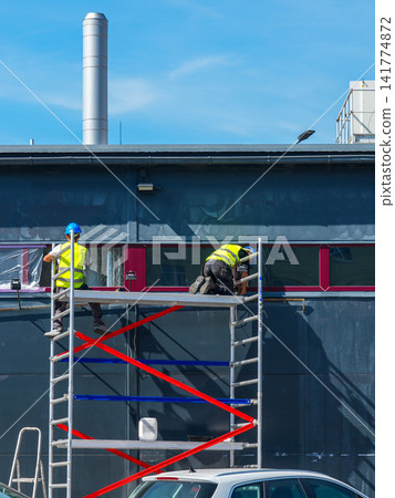 Construction Workers Installing Window Film from Mobile Scaffold on Modern Commercial Building Facade Construction Workers Installing Window Film from Mobile Scaffold on Modern Commercial Building Facade 141774872