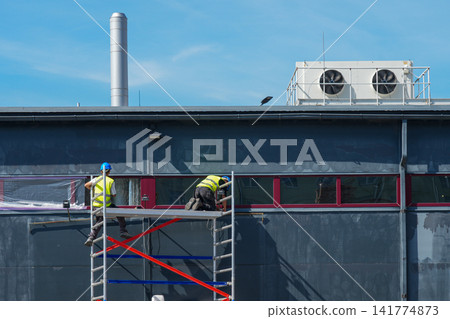 Construction Workers Installing Exterior Window Film from Mobile Scaffold on Commercial Building Facade Construction Workers Installing Exterior Window Film from Mobile Scaffold on Commercial Building Facade 141774873