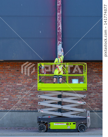 Construction Worker Painting Steel Column from Scissor Lift at Commercial Building Exterior Facade Construction Worker Painting Steel Column from Scissor Lift at Commercial Building Exterior Facade 141774877
