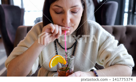 Casual Woman Drinks With Lemon. Closeup Of Woman Sipping Citrus Drink. Woman In City Cafe Enjoys Refreshing Citrus Beverage. Casual City Scene Showing Woman Delighting In Lemoninfused Drink Casual Woman Drinks With Lemon. Closeup Of Woman Sipping Citrus Drink. Woman In City Cafe Enjoys Refreshing Citrus Beverage. Casual City Scene Showing Woman Delighting In Lemoninfused Drink 141775374