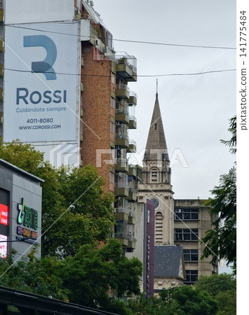 Buenos Aires, Argentina - March 28, 2026: Church Spire Rising Between Urban Buildings and Billboard Buenos Aires, Argentina - March 28, 2026: Church Spire Rising Between Urban Buildings and Billboard 141775484