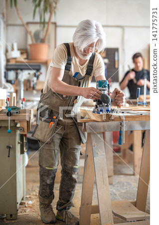 Carpenter works with handheld electric router machine on rail with additional stabilization handle. Carpenter works with handheld electric router machine on rail with additional stabilization handle. 141775731