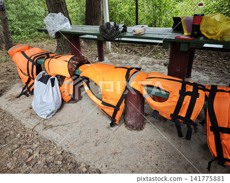 Bright orange life jackets arranged on wooden picnic bench Bright orange life jackets arranged on wooden picnic bench 141775881