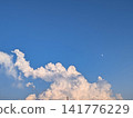 高聳的積雨雲在藍天中升起，白晝的月亮高懸 / 動態的夏日雲朵和漂浮的月亮（留白） 141776229
