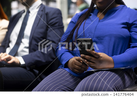 Close up of digital nomads in airport lobby checking flight information on smartphone. Freelancers doing business travel checking flight schedule details on mobile phone, sitting on chairs Close up of digital nomads in airport lobby checking flight information on smartphone. Freelancers doing business travel checking flight schedule details on mobile phone, sitting on chairs 141776404