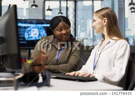 Cheerful IT specialist teaching intern to use artificial intelligence. African american woman guiding junior dev through AI tool integration, mentoring her on using machine learning APIs Cheerful IT specialist teaching intern to use artificial intelligence. African american woman guiding junior dev through AI tool integration, mentoring her on using machine learning APIs 141776435