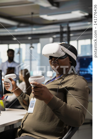 Software developer wearing VR goggles at office desk developing programs using AI automation. African american IT expert using virtual reality, debugging applications with artificial intelligence Software developer wearing VR goggles at office desk developing programs using AI automation. African american IT expert using virtual reality, debugging applications with artificial intelligence 141776436