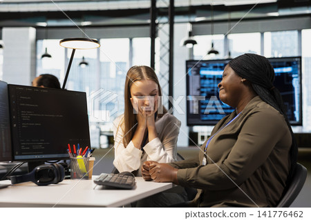 Worried employee sharing concerns with empathetic team leader at desk offering empathetic encouragement. African american woman helping sad coworker, offering comfort in office 141776462