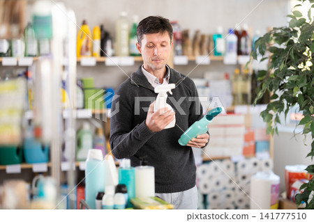Positive male shopper carefully selects spray glass cleaner for windows in her home Positive male shopper carefully selects spray glass cleaner for windows in her home 141777510