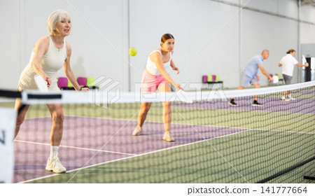 Womens playing pickleball tennis on the pickleball court indoors Womens playing pickleball tennis on the pickleball court indoors 141777664