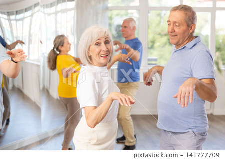 Smiling senior woman dancing twist with man in dance studio Smiling senior woman dancing twist with man in dance studio 141777709