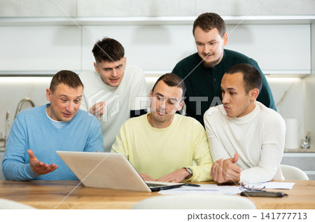 Group of men discussing with paperwork and laptop at home kitchen Group of men discussing with paperwork and laptop at home kitchen 141777713